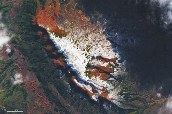 Reddish orange vegetation covers the slopes of a snow-capped mountain in southern Chile. The mountain drops off steeply toward a river valley on the left side and slopes more gently to the right.